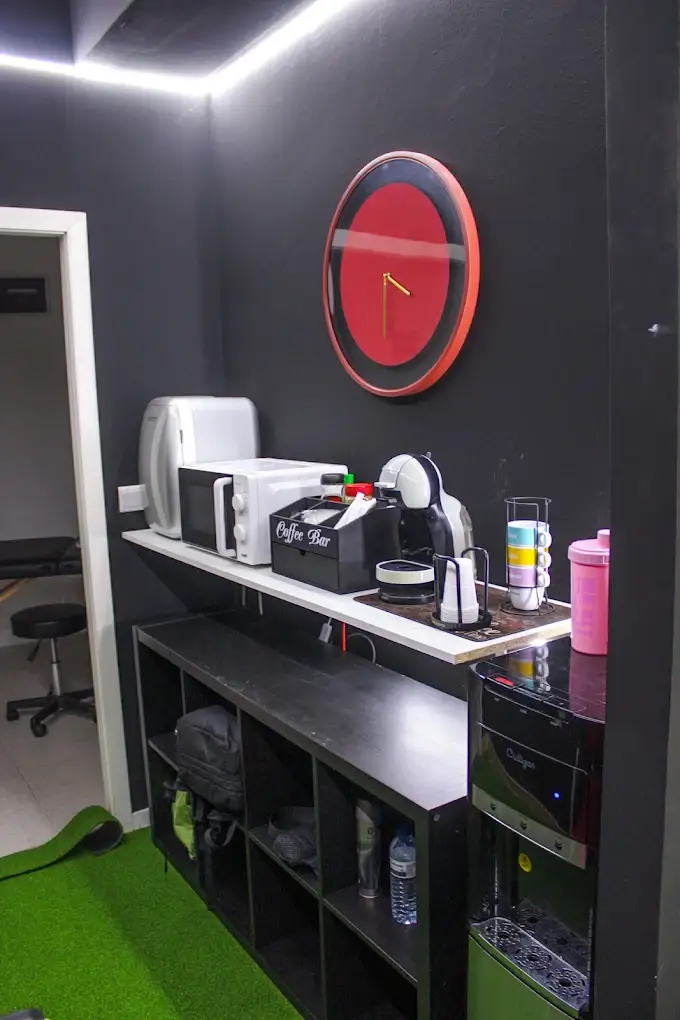 Zona de apoio com coffee bar, dispensador de água e relógio vermelho na parede preta